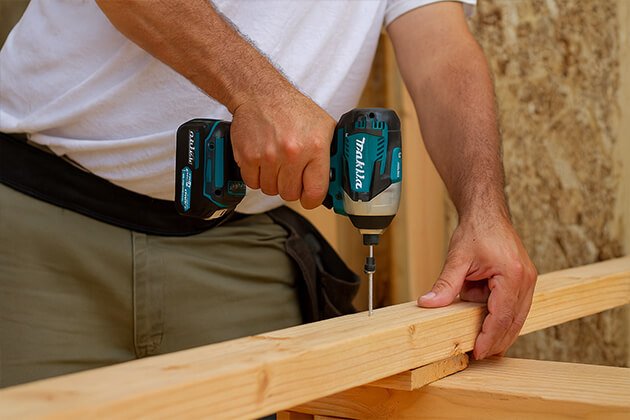 Ouvrier utilisant une visseuse à chocs sans fil Makita 18V pour assembler une structure en bois