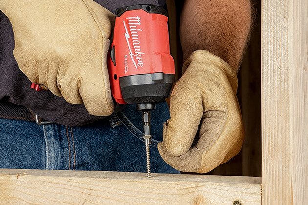 Travailleur avec gants utilisant une visseuse à chocs sans fil Milwaukee M18 Fuel pour visser dans du bois