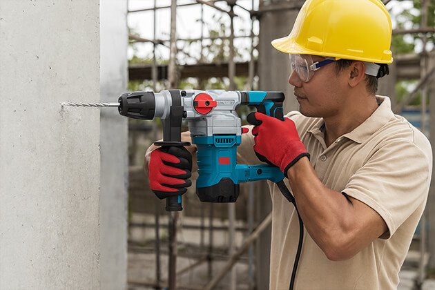 Ouvrier avec casque de protection utilisant un perforateur burineur filaire Eneacro pour percer un mur en béton sur chantier, outil électroportatif puissant pour maçonnerie