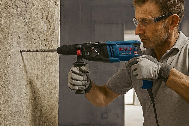 Ouvrier utilisant un perforateur burineur filaire Bosch Professional GBH pour percer un mur en béton, outil électroportatif puissant de chantier