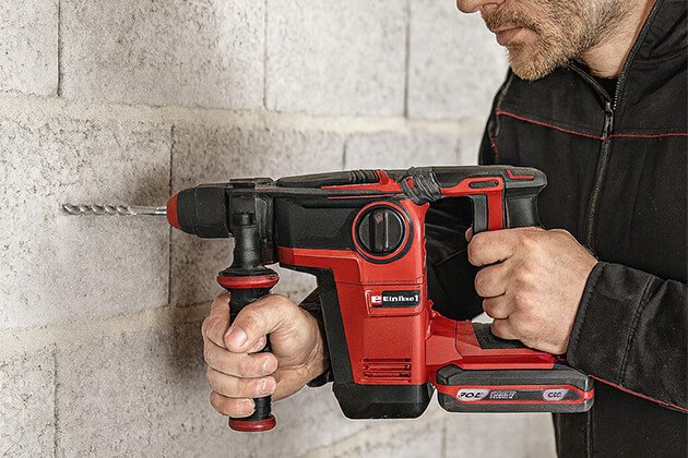 Ouvrier utilisant un perforateur burineur sans fil Einhell Professional 18V pour percer un mur en parpaing, outil électroportatif puissant pour béton et maçonnerie